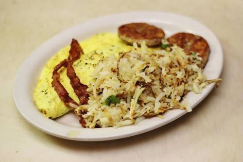 A plate of breakfast featuring an omelet, crispy bacon, hash browns, and sausage patties.