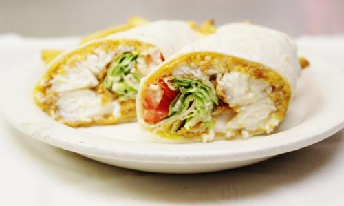 A plate with two halves of a fish wrap filled with lettuce, tomato, and sauce, served with fries.
