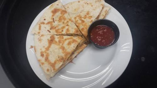 A plate with sliced quesadilla pieces and a small cup of salsa on the side.