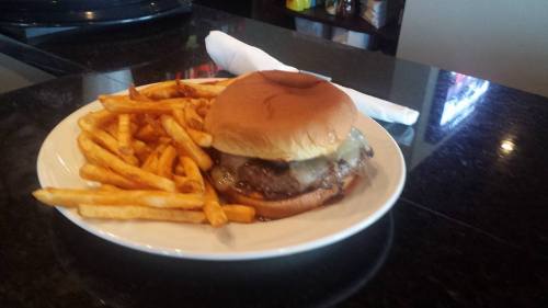 A juicy burger with melted cheese on a bun, served with a side of crispy French fries on a white plate.