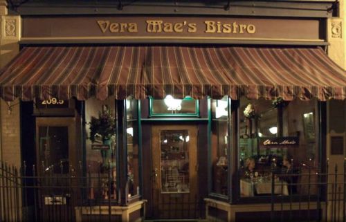 Exterior of Vera Mae's Bistro, featuring a striped awning and warmly lit windows, inviting diners inside.