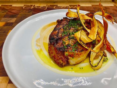 A beautifully plated dish featuring a grilled meat cut topped with crispy vegetables and drizzled with sauce.