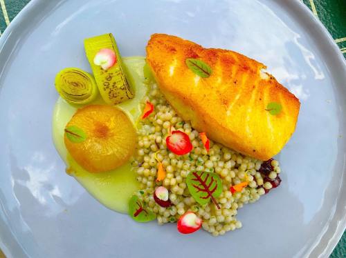 A beautifully plated dish featuring grilled fish, couscous, and colorful vegetables on a light blue plate.