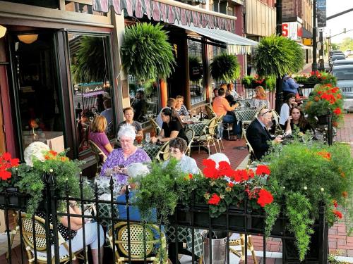 Outdoor dining scene with people at tables surrounded by vibrant flowers and greenery, enjoying a lively atmosphere.