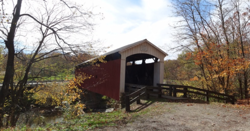 A red and white covered bridge surrounded by autumn trees and a clear blue sky.