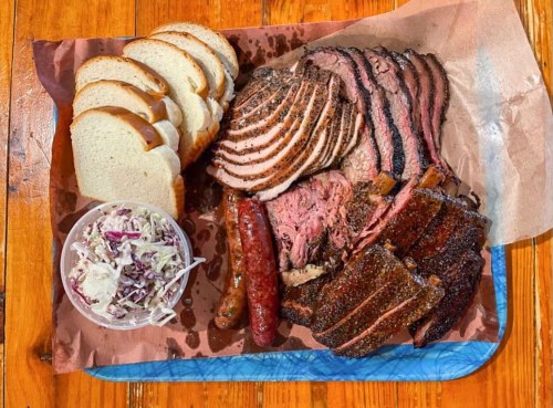 A platter of assorted smoked meats, including brisket and sausage, served with slices of bread and a side of coleslaw.