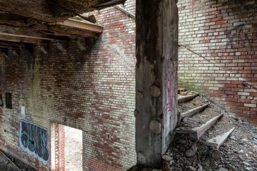 Abandoned building interior with exposed brick walls, graffiti, and crumbling stairs leading to a doorway.