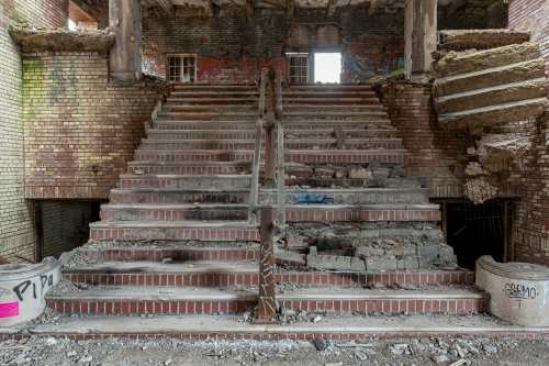 Abandoned building interior featuring crumbling brick stairs with graffiti and debris scattered around.