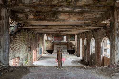 Interior of a dilapidated building with exposed brick, crumbling walls, and a staircase leading to an upper level.