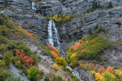 A waterfall cascades down rocky cliffs, surrounded by vibrant autumn foliage in shades of red, orange, and yellow.