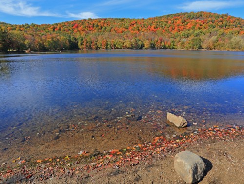 A serene lake surrounded by vibrant autumn foliage, with colorful leaves reflecting on the water's surface.