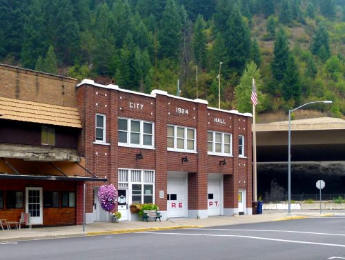 Historic brick city hall building with "1924" and "CITY HALL" signs, surrounded by trees and a quiet street.