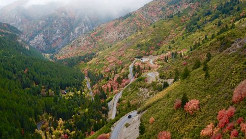 Aerial view of winding road through colorful autumn foliage in a mountainous landscape.