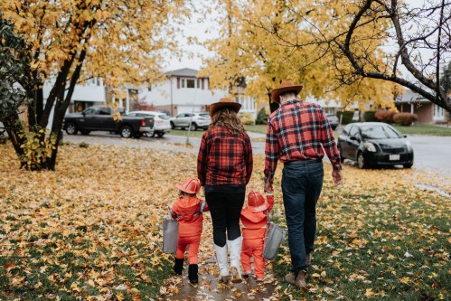 A family in matching plaid shirts and orange outfits walks through a leaf-covered street in autumn.