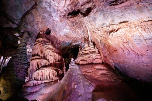Stalactites and stalagmites in a colorful cave, illuminated by soft lighting, showcasing unique rock formations.