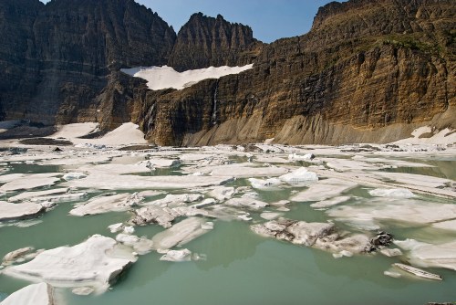 A glacial landscape featuring icebergs floating in a turquoise lake, surrounded by towering rocky cliffs.