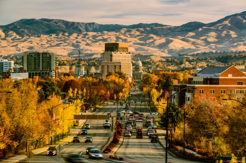 A scenic view of a city in autumn, with colorful trees lining the streets and mountains in the background.