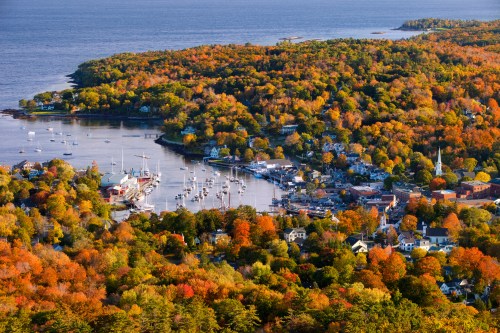 Aerial view of a coastal town surrounded by vibrant autumn foliage and a harbor filled with boats.