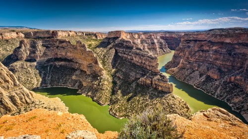 A stunning canyon landscape with steep cliffs and a winding green river under a clear blue sky.