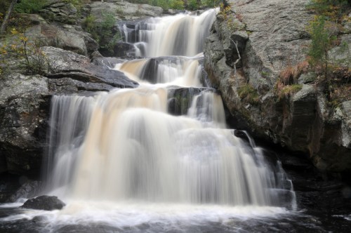 A serene waterfall cascading over rocky terrain, surrounded by lush greenery and smooth stones.