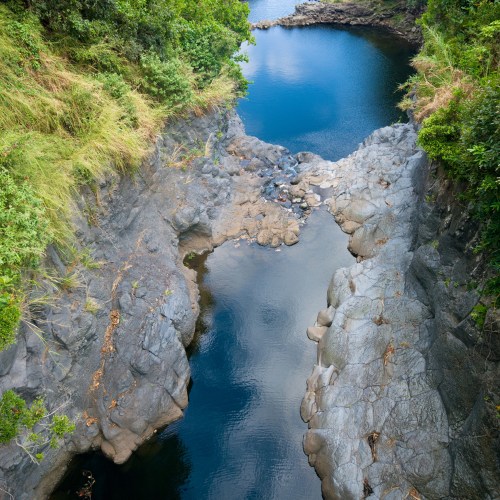 A serene river flows between rocky banks, surrounded by lush greenery and calm blue waters.