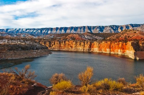 A serene lake surrounded by colorful cliffs and mountains under a cloudy sky.