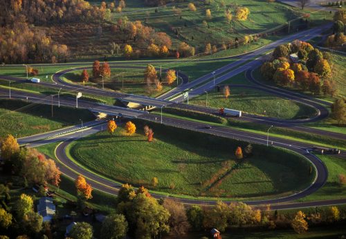Aerial view of a highway interchange surrounded by autumn trees and green fields.
