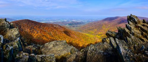 Panoramic view of colorful autumn mountains, with rocky foreground and vibrant foliage stretching across the landscape.