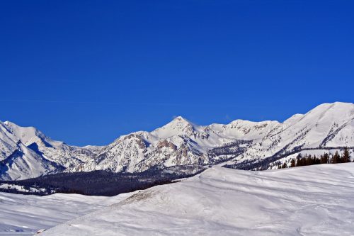 Snow-covered mountains under a clear blue sky, with a vast expanse of white terrain in the foreground.