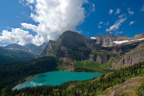 A stunning mountain landscape featuring a turquoise lake surrounded by lush forests and towering peaks under a blue sky.
