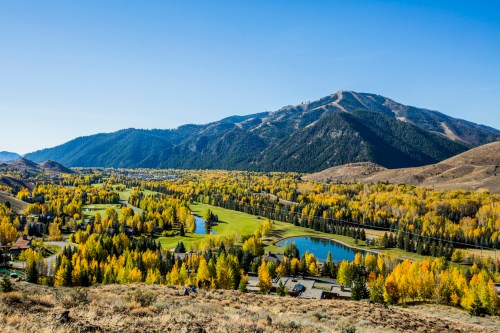 A scenic view of a valley with vibrant autumn foliage, mountains in the background, and a serene pond.