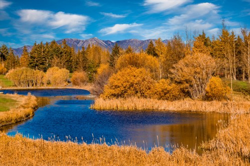 A serene landscape featuring a winding river surrounded by autumn foliage and mountains under a blue sky.