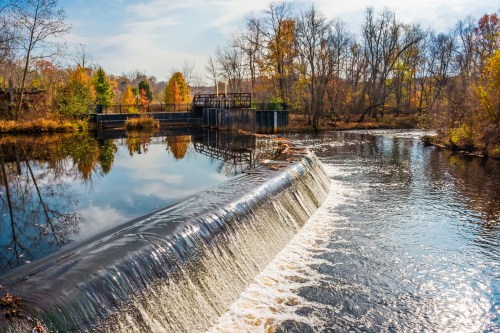 A serene river scene with a waterfall, surrounded by autumn trees and a clear blue sky.