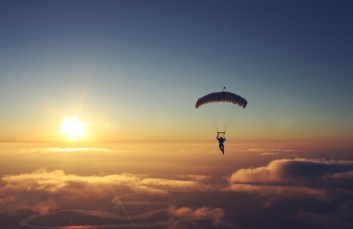 A person parachuting through the sky at sunset, surrounded by clouds and a winding river below.