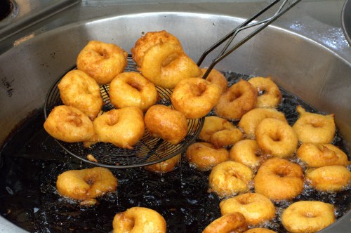 A metal strainer lifts freshly fried golden donuts from a pot of bubbling oil.