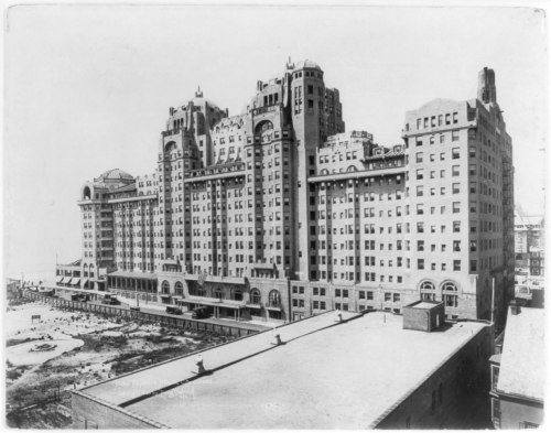 Historic black-and-white photo of a large, ornate hotel building by the beach, showcasing its architectural details.