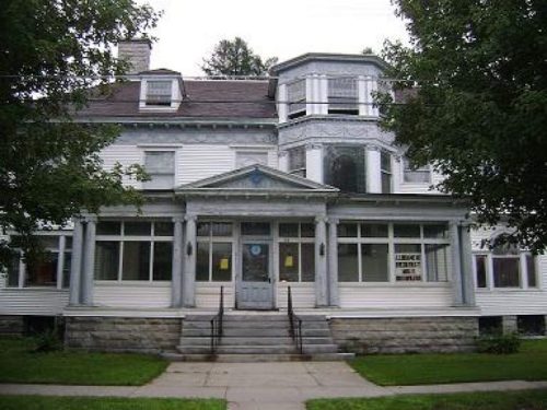 A large, historic house with a decorative facade, columns, and a prominent entrance, surrounded by trees and grass.