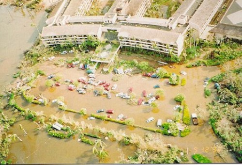 Aerial view of a flooded area with submerged cars and a damaged building surrounded by water and debris.
