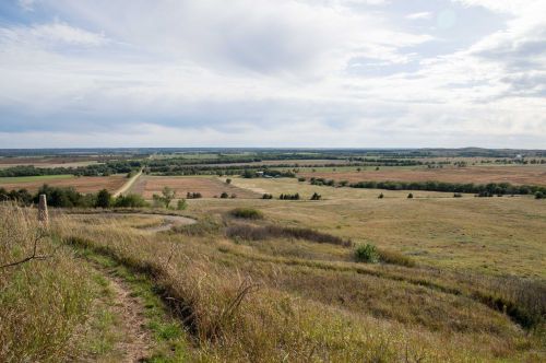 A scenic view of rolling hills and fields under a cloudy sky, with a winding road cutting through the landscape.