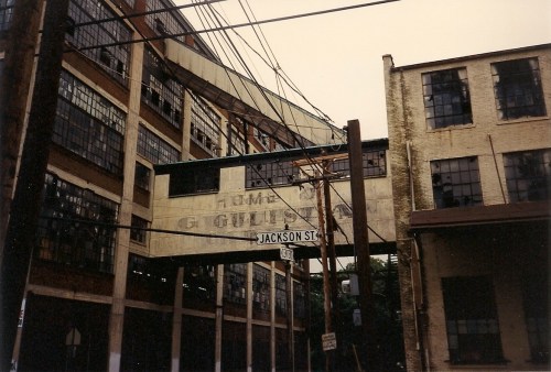 Abandoned industrial buildings with large windows and a street sign for Jackson St, surrounded by power lines.