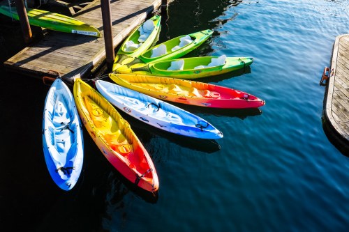 Colorful kayaks arranged in a circle on calm water, with a wooden dock in the background.