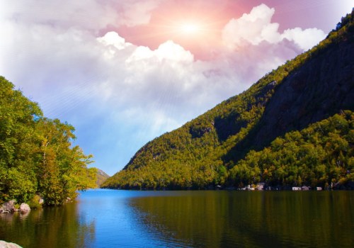 A serene lake surrounded by lush green mountains under a bright sky with soft clouds and sunlight.