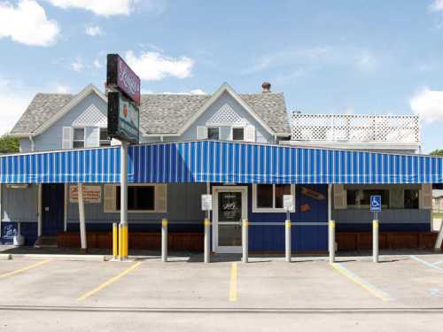 A blue-striped awning covers the entrance of a quaint restaurant with a sign, surrounded by parking spaces.