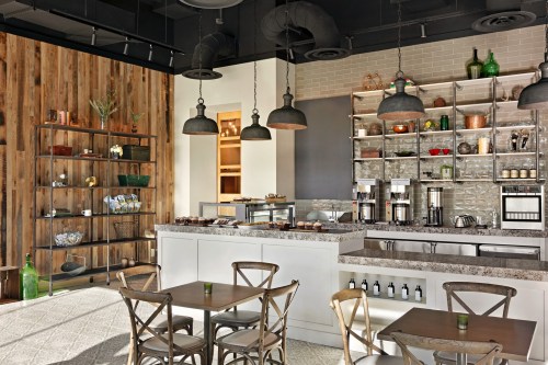 Modern café interior featuring a sleek counter, shelves with decor, and wooden accents, with tables and chairs for seating.