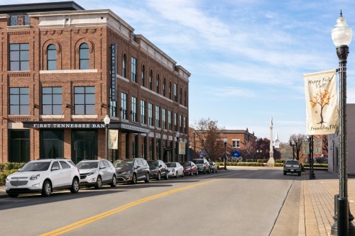 A street view featuring a brick building with "First Tennessee Bank" signage and parked cars along the road.