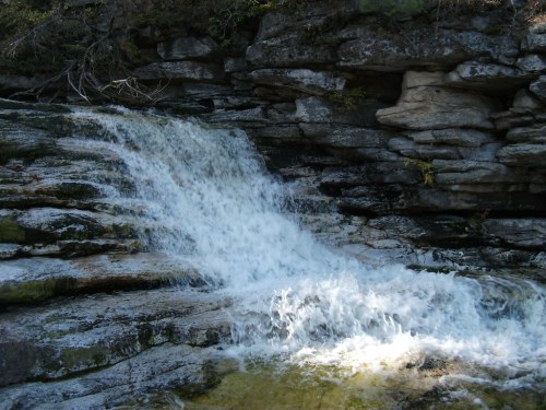 A small waterfall cascading over rocky terrain, surrounded by greenery and natural stone formations.