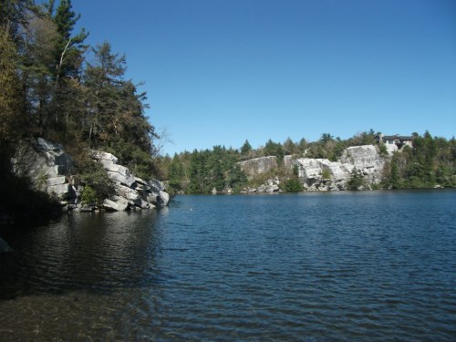 A serene lake surrounded by rocky cliffs and lush trees under a clear blue sky.