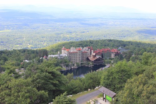 Aerial view of a large hotel surrounded by lush green trees and mountains in the background.