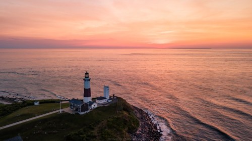 A scenic view of a lighthouse on a cliff at sunset, with calm ocean waters and a colorful sky.
