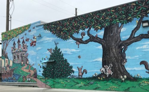 Colorful mural featuring a whimsical castle, tree, and playful animals against a blue sky backdrop.